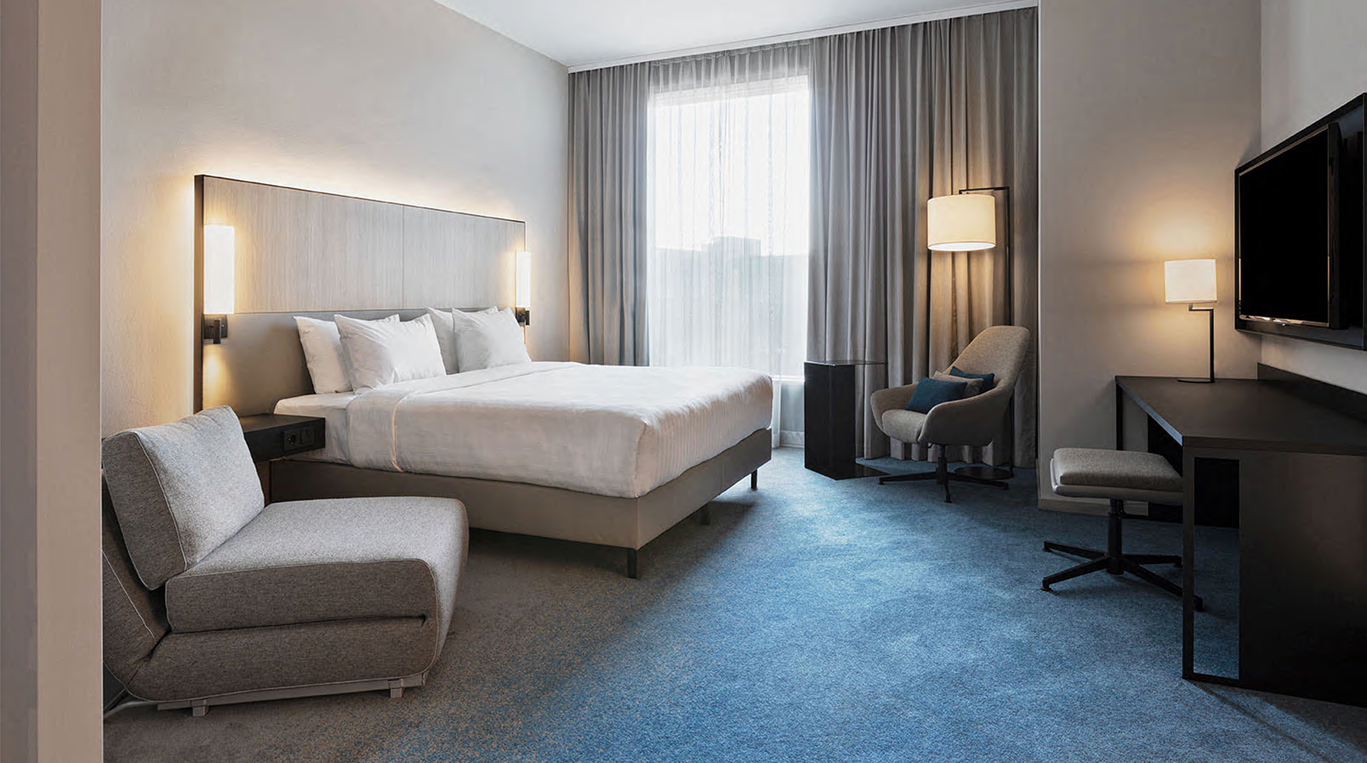 Modernes Hotelzimmer mit Bett, Sesseln und Fernseher