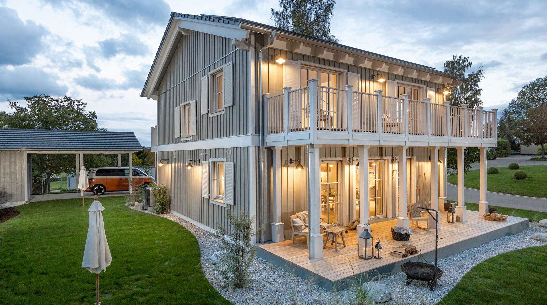 Die Rückseite des Hauses mit Terrasse und Garten. Die Hälfte der Terrasse ist durch eine Balkon überdacht