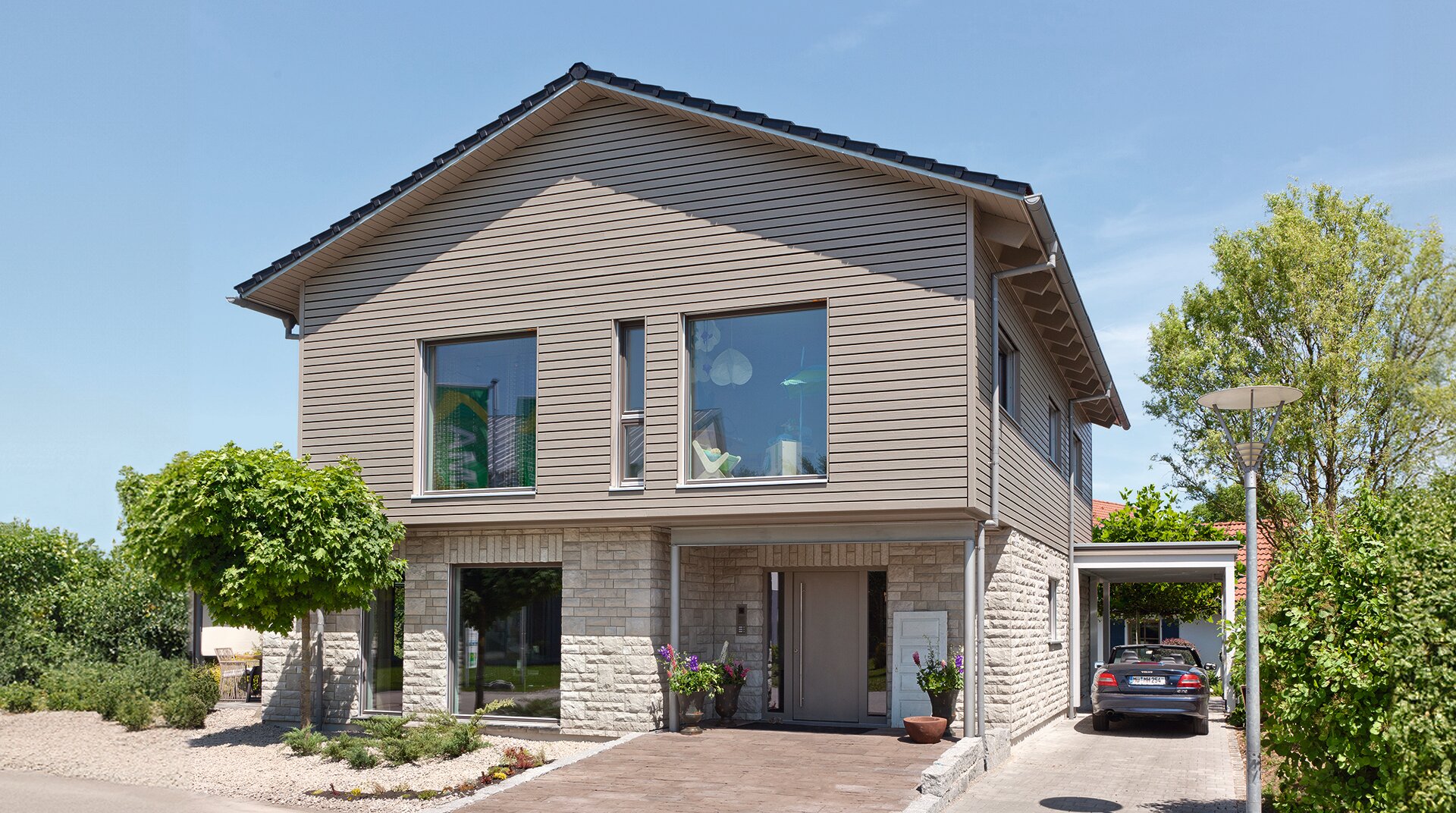 Frontansicht des Hauses mit Carport und großem Eingangsbereich. Große Fenster lassen viel Licht in das Gebäude